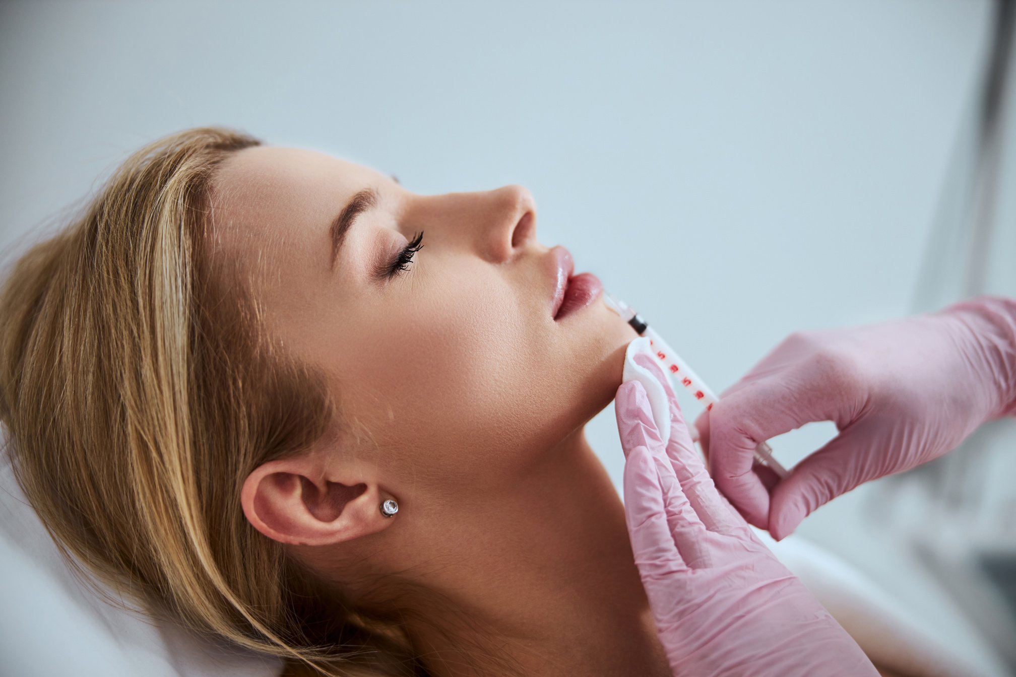 Professional cosmetologist injecting a dermal filler into the patient lips